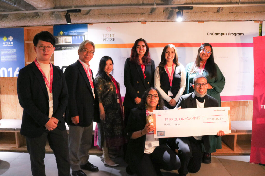 The two members of Team Tikbal is kneeling and holding a giant symbolic check worth JPY 150,000. The chief guests and judges are standing up. They are posing for the photo.
