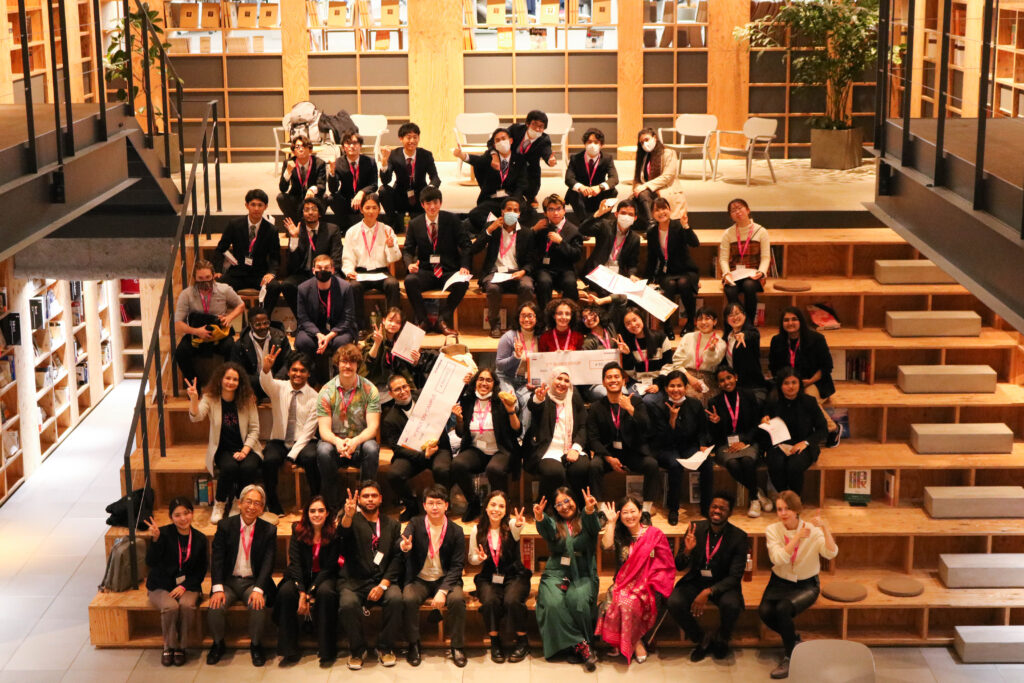 Student competitors, judges, guests, OC members, and volunteers of the Hult Prize are sitting on the bleachers, posing for the photo.