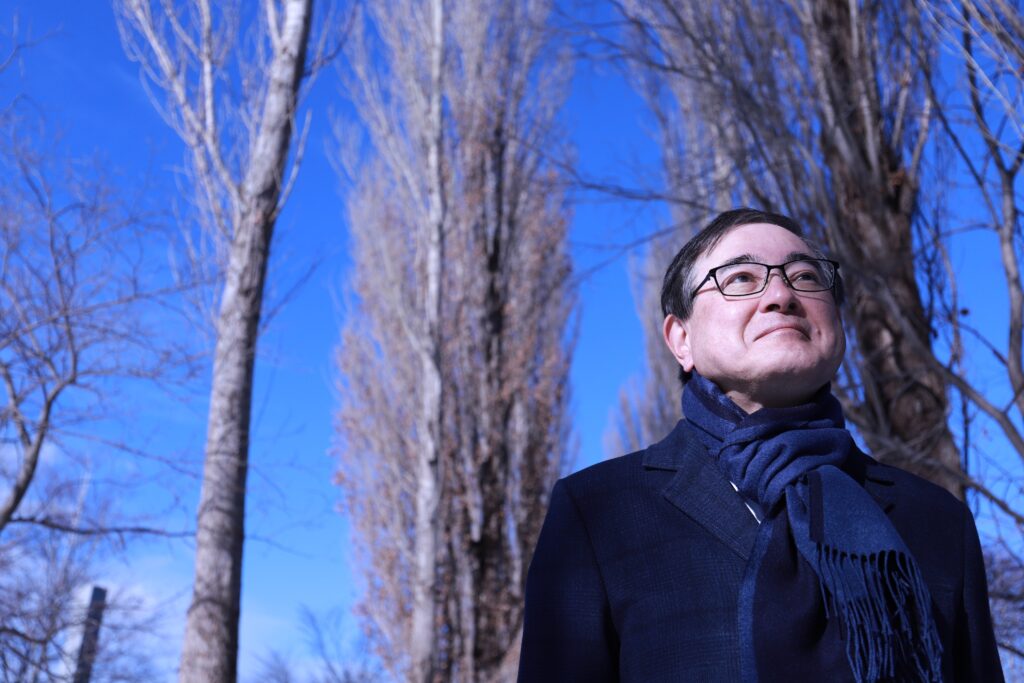President Kiyohiro Houkin is standing between rows of poplar trees, looking above.