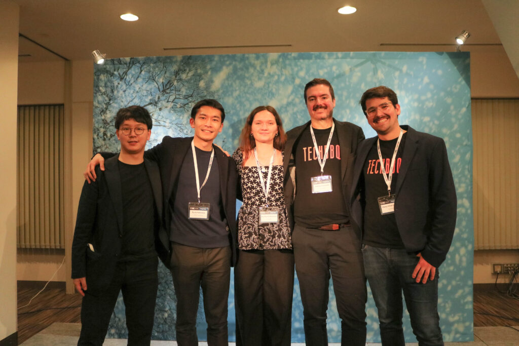 Five people dressed in black are standing in front of the event's main standing banner, posing for the photo.