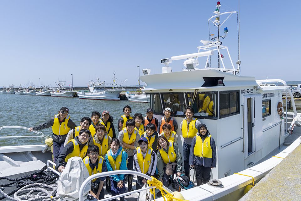 A group of students, all wearing yellow life vests, standing in the training vessel posing for a photo.
