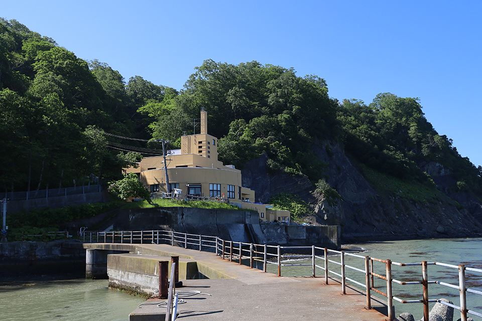 The yellow building of Akkeshi marine station surrounded by the cliffs taken from the pier.