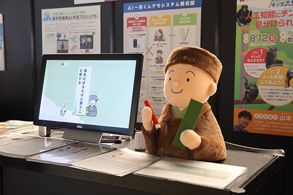 A mascot plushie of Issa-kun being displayed on top of a table next to a computer screen. The screen is displaying Issa-kun's haiku.