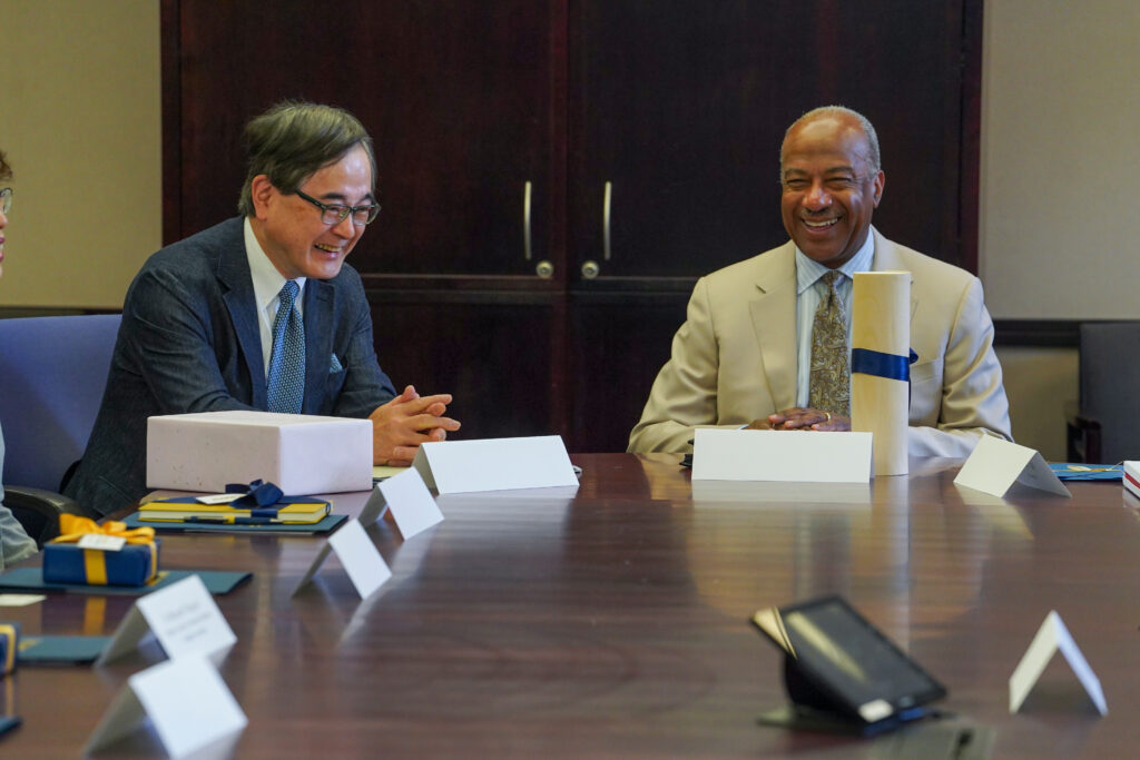 President Houkin and Chancellor May sitting on a desk laughing