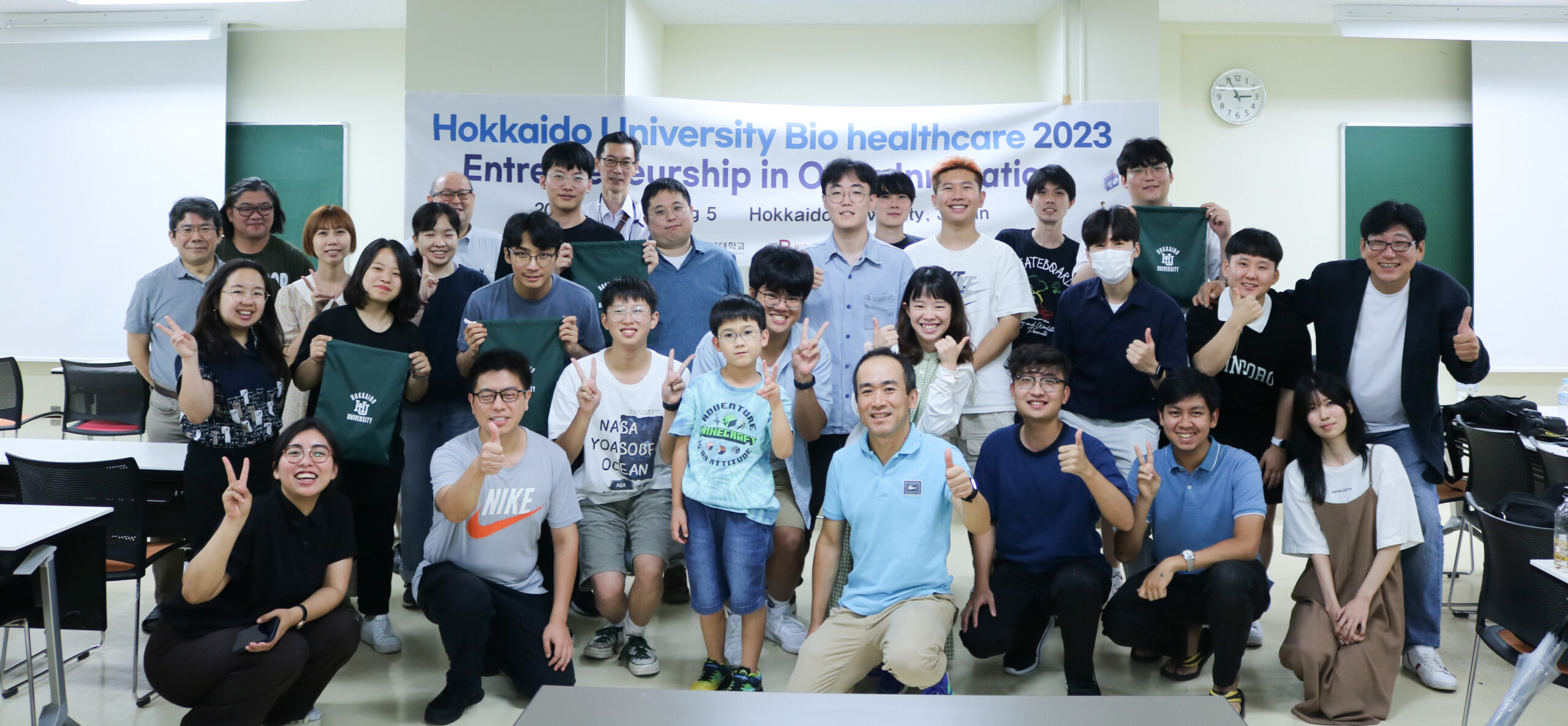 Student participants, lecturers, and organizers of the workshop are lined up in front of the workshop banner posing for the photo.