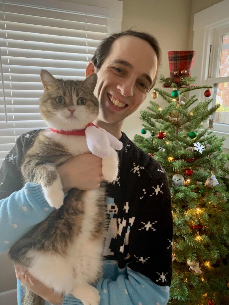 Alexander Pettitt with his family cat, Freyja, in front of a real Christmas tree.